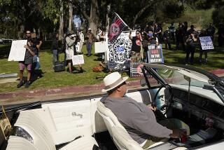 A driver passes a small group of anti-vaccine protesters outside the vaccine distribution site at Dodger Stadium on Saturday.