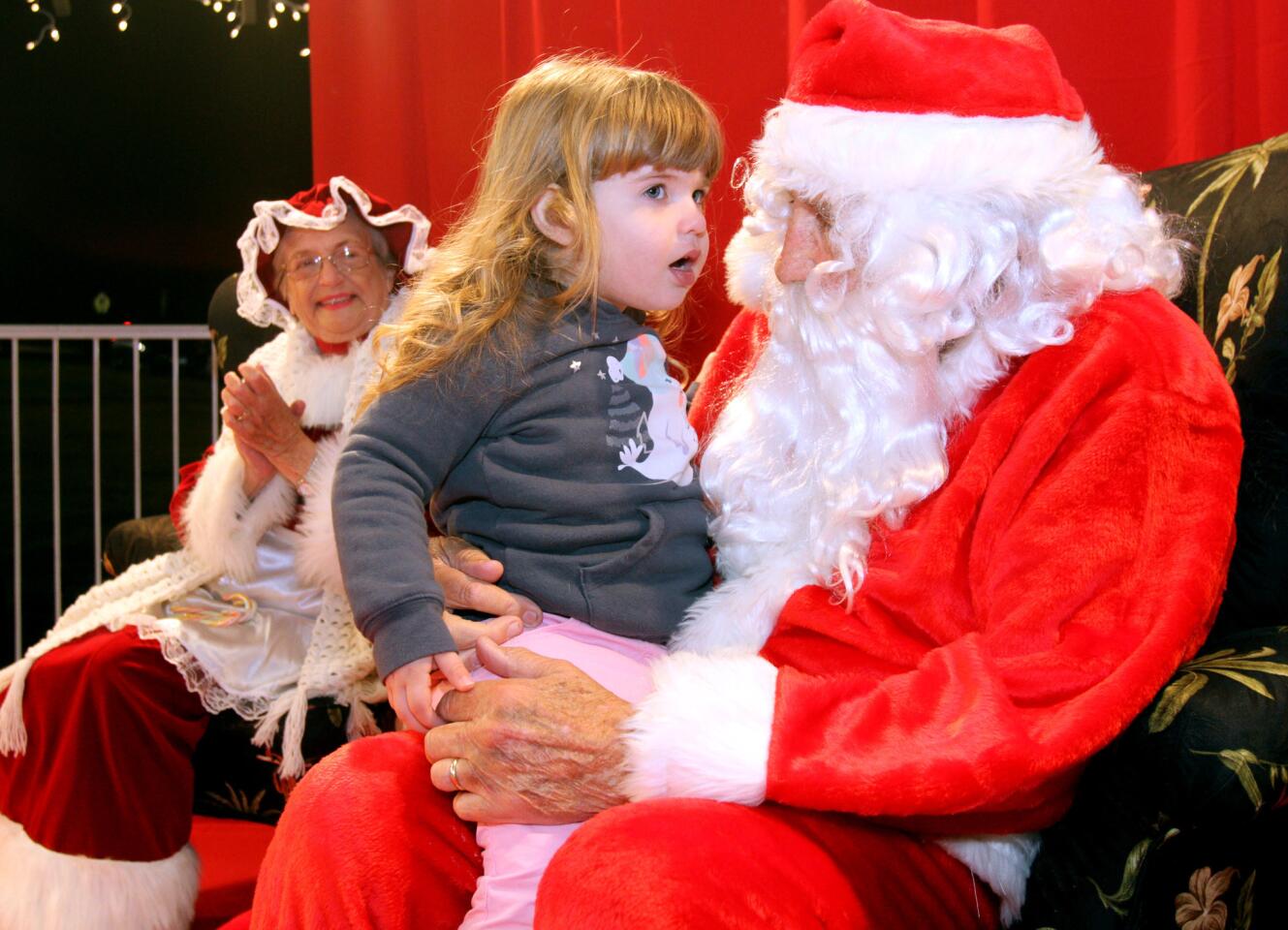 With Mrs. Claus in the background, Juliette Berg, 3 of Glendale, tells Santa Claus what she would like for Christmas during the 21st Festival in Lights at Memorial Park in La Cañada Flintridge on Friday, December 4, 2015. Santa also turned on the lights at the park's gazebo.