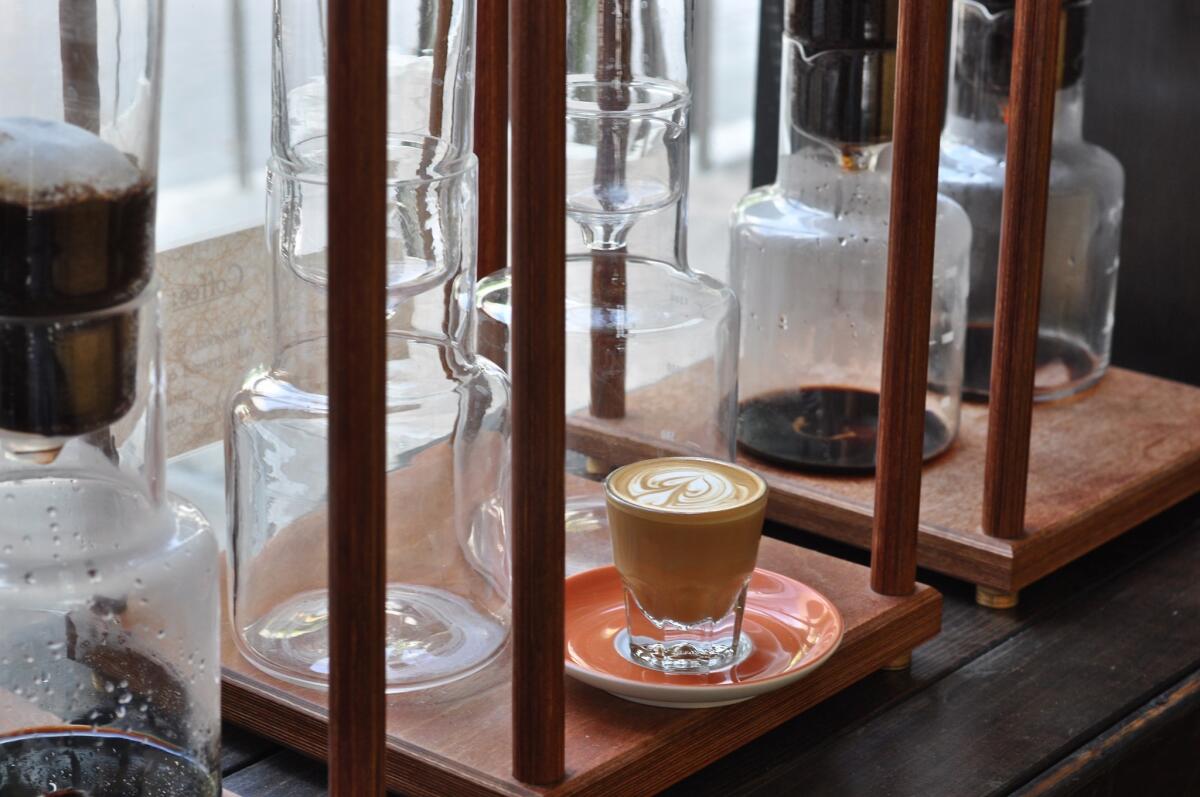 A cortado sits near the row of siphon coffeemakers brewing cold drip coffee at the Cafe Demitasse in Little Tokyo.