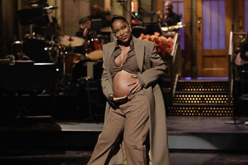 A woman in a brown trench coat showing off her baby bump on a stage