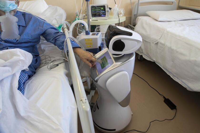 A coronavirus patient under treatment in the intensive care unit uses the touch screen of a robot at 'Ospedale di Circolo' hospital, in Varese, Italy, Wednesday, April 8, 2020. Six robots help healthcare professionals assist Covid-19 patients, one robot for every two patients to maximize monitoring and assistance. The new coronavirus causes mild or moderate symptoms for most people, but for some, especially older adults and people with existing health problems, it can cause more severe illness or death. (AP Photo/Luca Bruno)