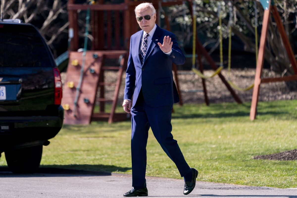 President Biden, in a blue suit and sunglasses, waves.