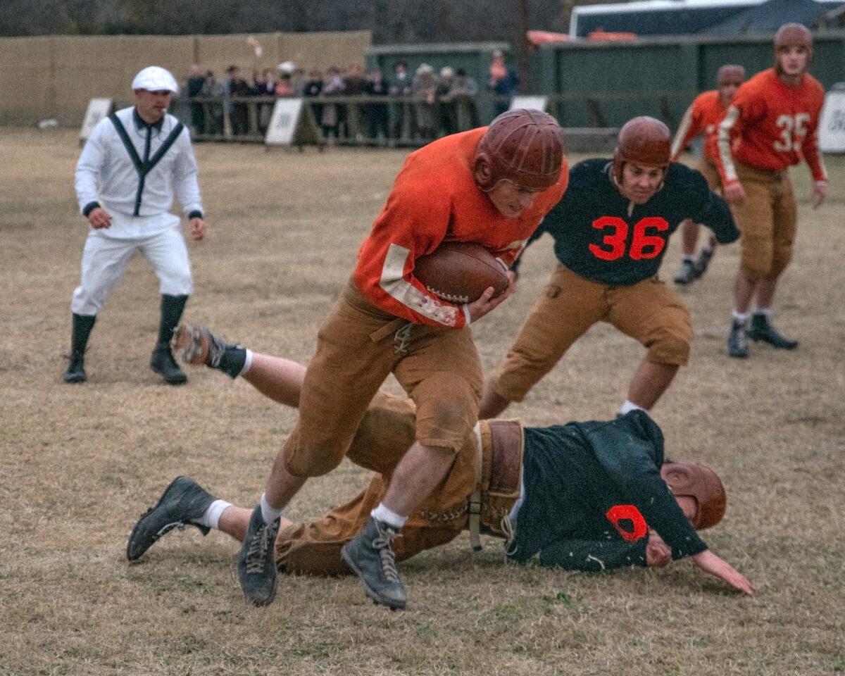 A young man in an old-time football uniform charges up the field while evading tacklers.
