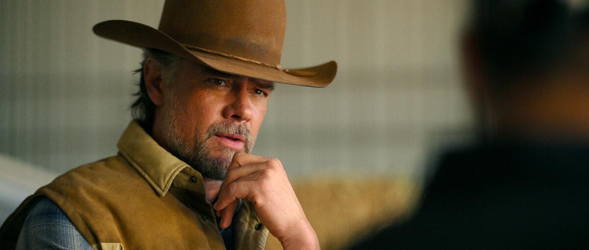 A man wearing a cowboy hat places his hand on his chin.