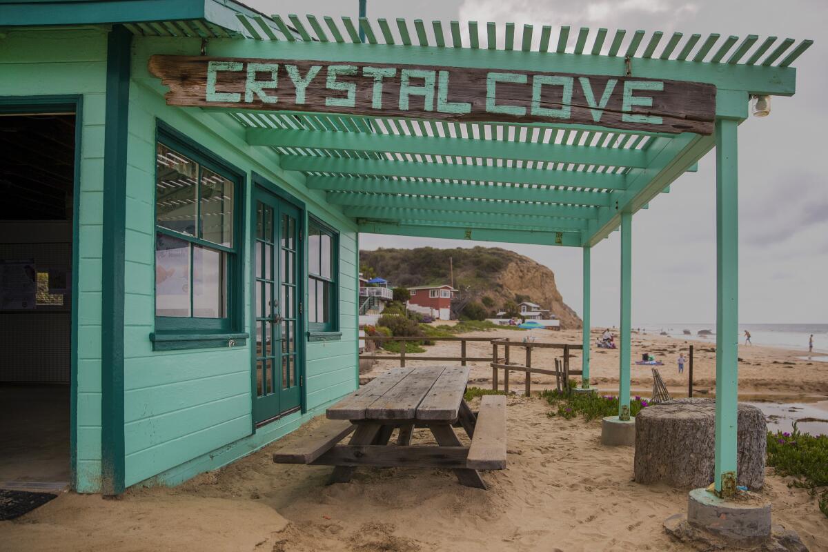 Beachgoers explore the beach near the historic blue-green cottage at Crystal Cove.