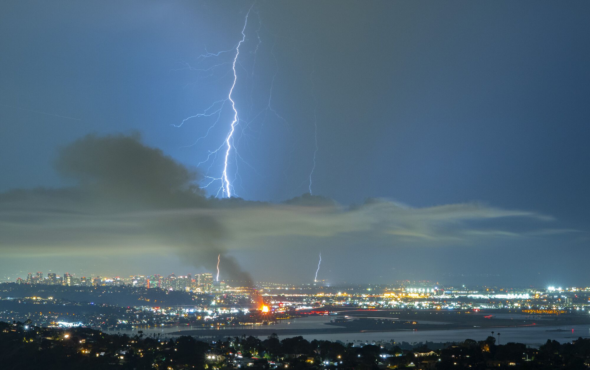 Lighting strikes the ground in San Diego as a palm trees burn from a lightning strike in the Morena area.