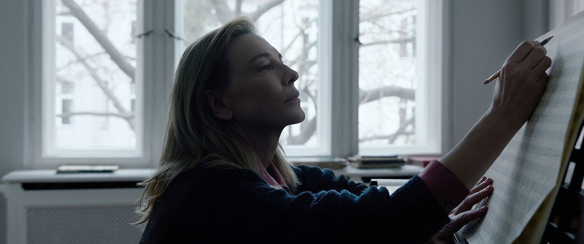 Cate Blanchett sits at a piano and writes on sheet music in  “Tár.”