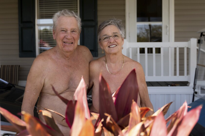 In this image provided by the Religion News Service , Bill and Misty Katz pose in front of their home at Nature's Resort on March 16, 2022, in Elsa, Texas. Bright orange letters welcome you to “Nature’s Resort.” Nothing looks amiss, except for what’s missing — clothing. (Jeremy Lindenfeld/Religion News Service via AP)