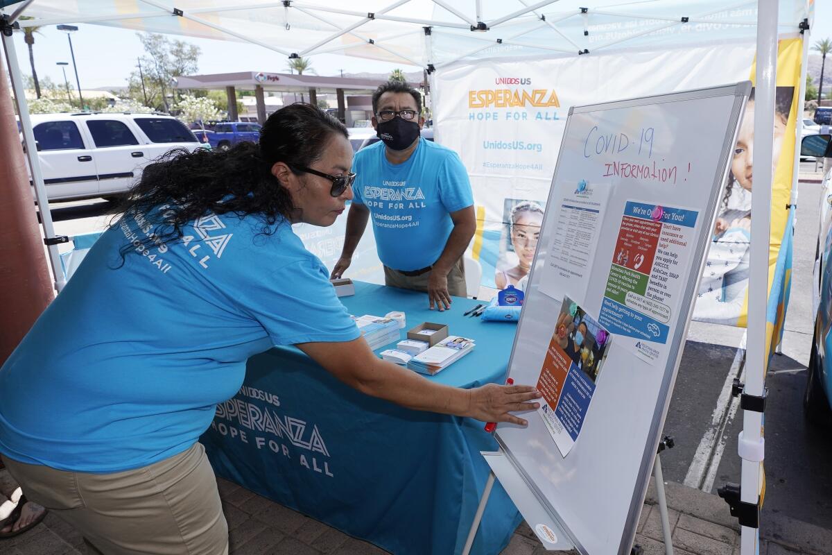 FILE - In this May 7, 2021, file photo, Sonia Lorenzana, left, and Jose Marquez, right, of UnidosUS, set up an informational tent display, increasing efforts to bring more vaccine doses into Latino neighborhoods, at a local shopping plaza in Phoenix. Latinos in the U.S. were hard hit by the pandemic both financially and personally, but many feel generally optimistic that the worst is behind them, according to a new study by the Pew Research Center. (AP Photo/Ross D. Franklin, File)