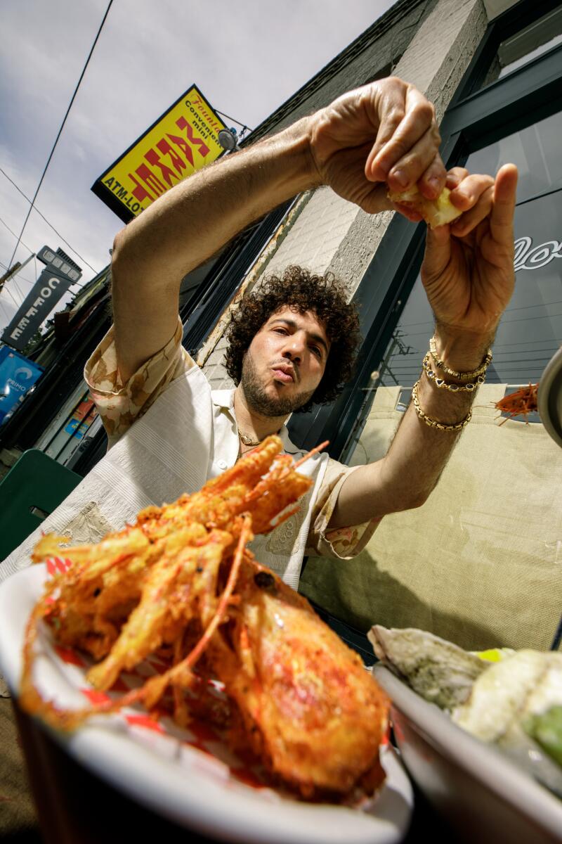 A low angle photo of Benny Blanco squeezing lemon onto some seafood.