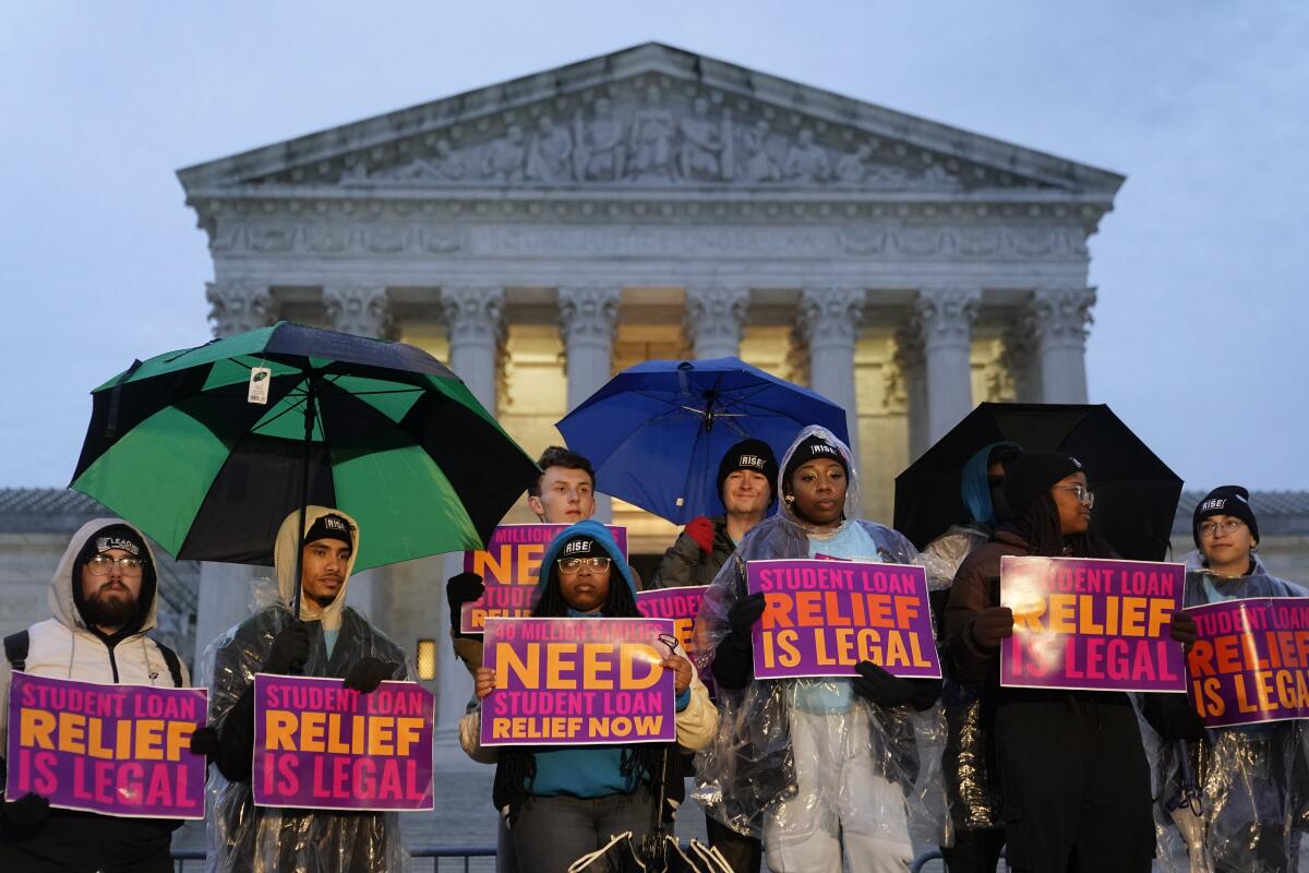 Student debt relief advocates hold umbrellas and signs in front of the Supreme Court
