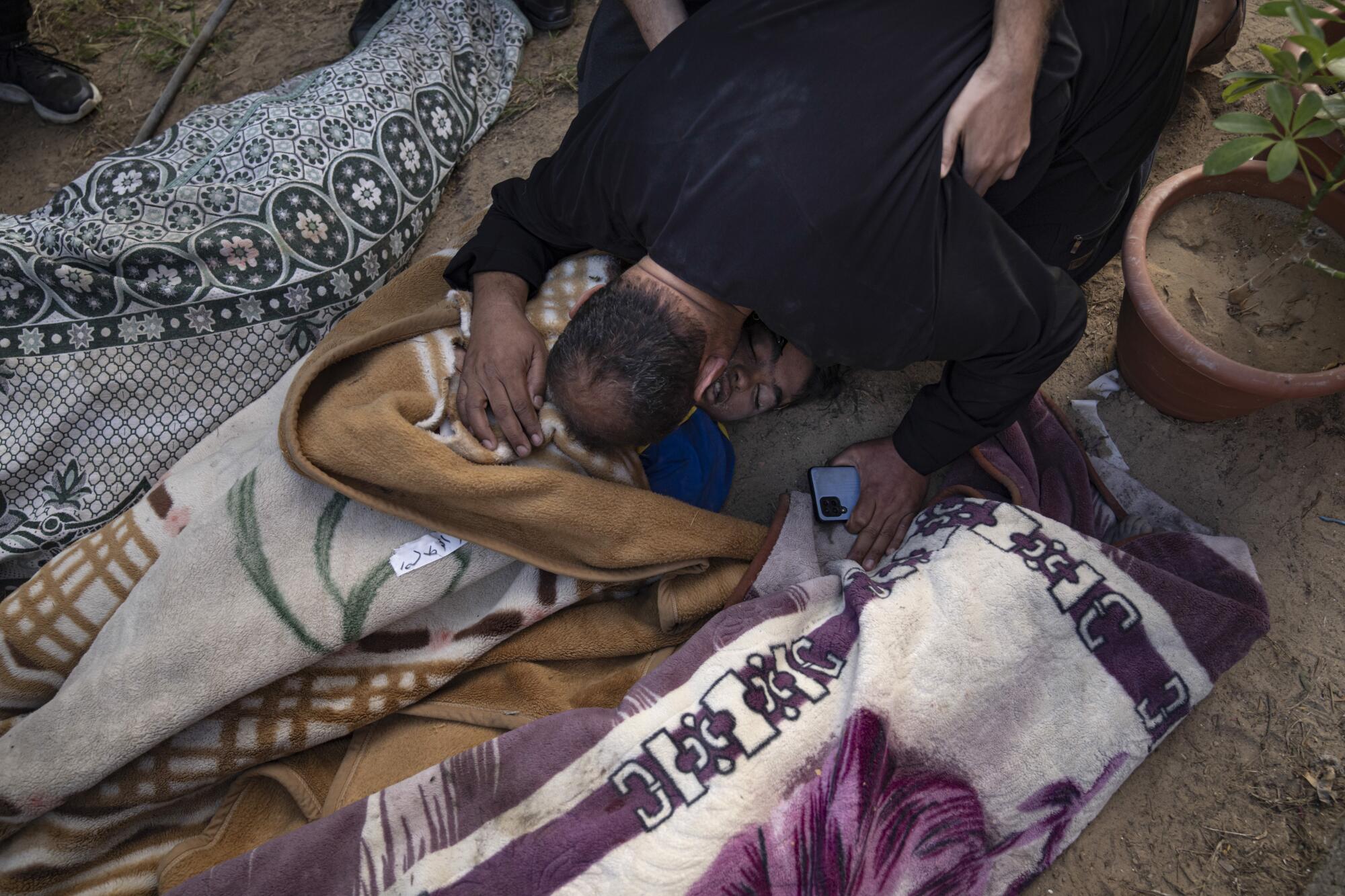 A Palestinian man bows in grief over bodies wrapped in blankets.