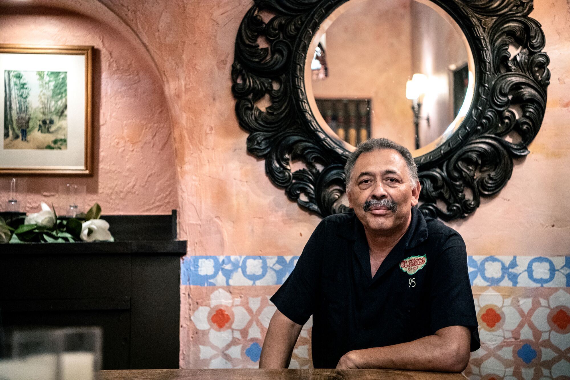 Jaime Cornelio sitting at a table, with a circular mirror on the wall behind him.