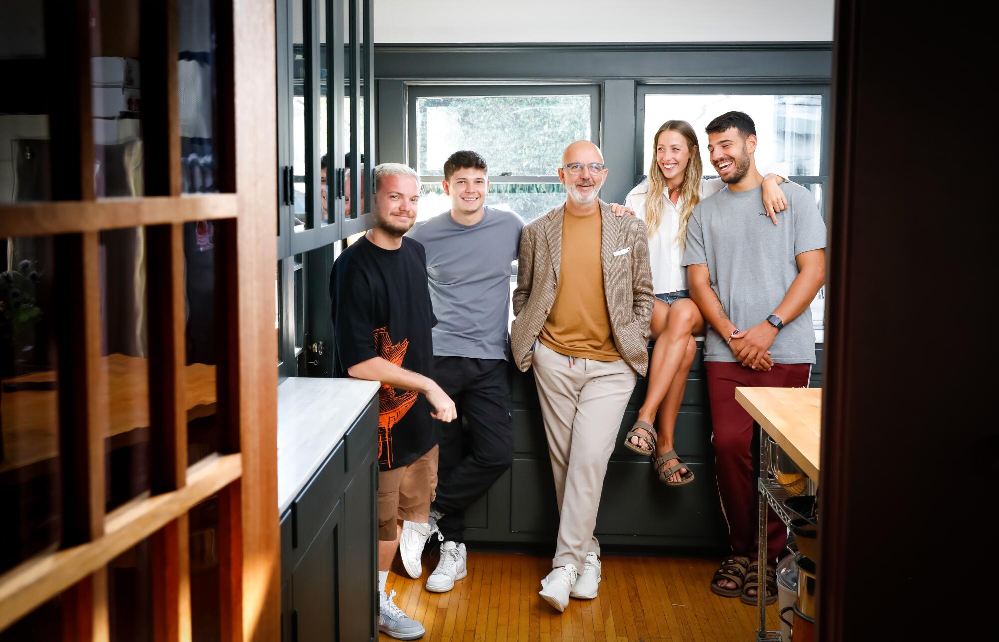 Three young men and a young woman flank an older man in a kitchen.