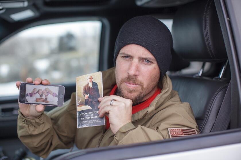 Jon Ritzheimer shows a family picture on his phone and a copy of a pocket Constitution at the Malheur National Wildlife Refuge Headquarters near Burns, Ore.