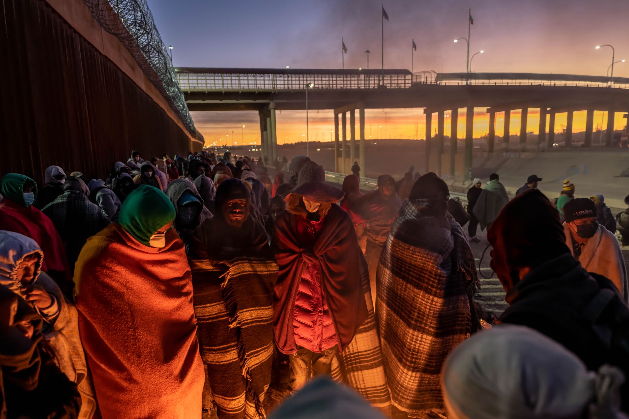  Immigrants wrapped in blankets gather around a fire 