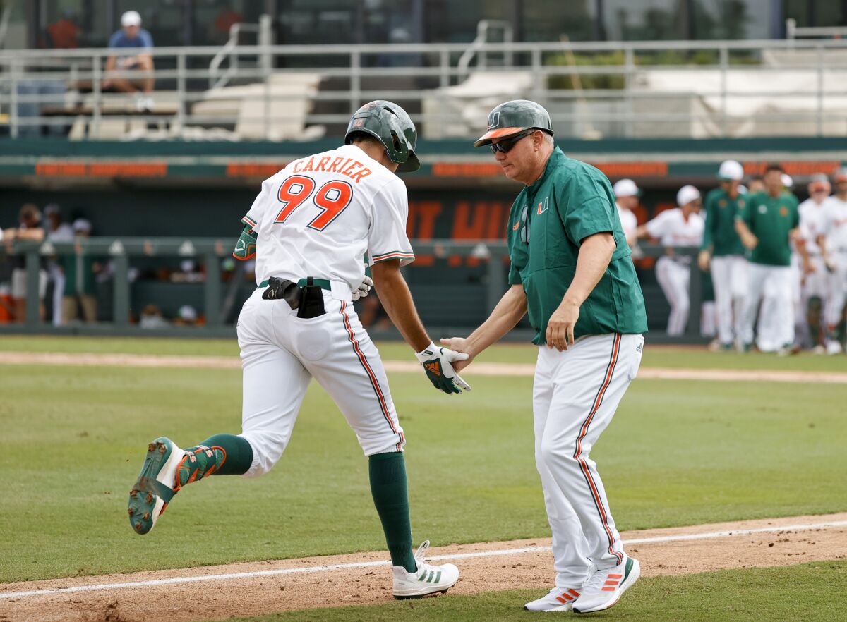FILE - Miami Hurricanes right fielder Lorenzo Carrier (99) is congratulated by Hurricanes head coach Gino DiMare after hitting a grand slam during the second inning of an NCAA baseball game against the Towson Tigers in Alex Rodriguez Park at Mark Light Field in Coral Gables, Fla., Sunday, Feb. 20, 2022. Miami is on its longest winning streak in coach Gino DiMare's four seasons and playing its best baseball since Jim Morris' 2016 team reached the College World Series. (David Santiago/Miami Herald via AP, File)