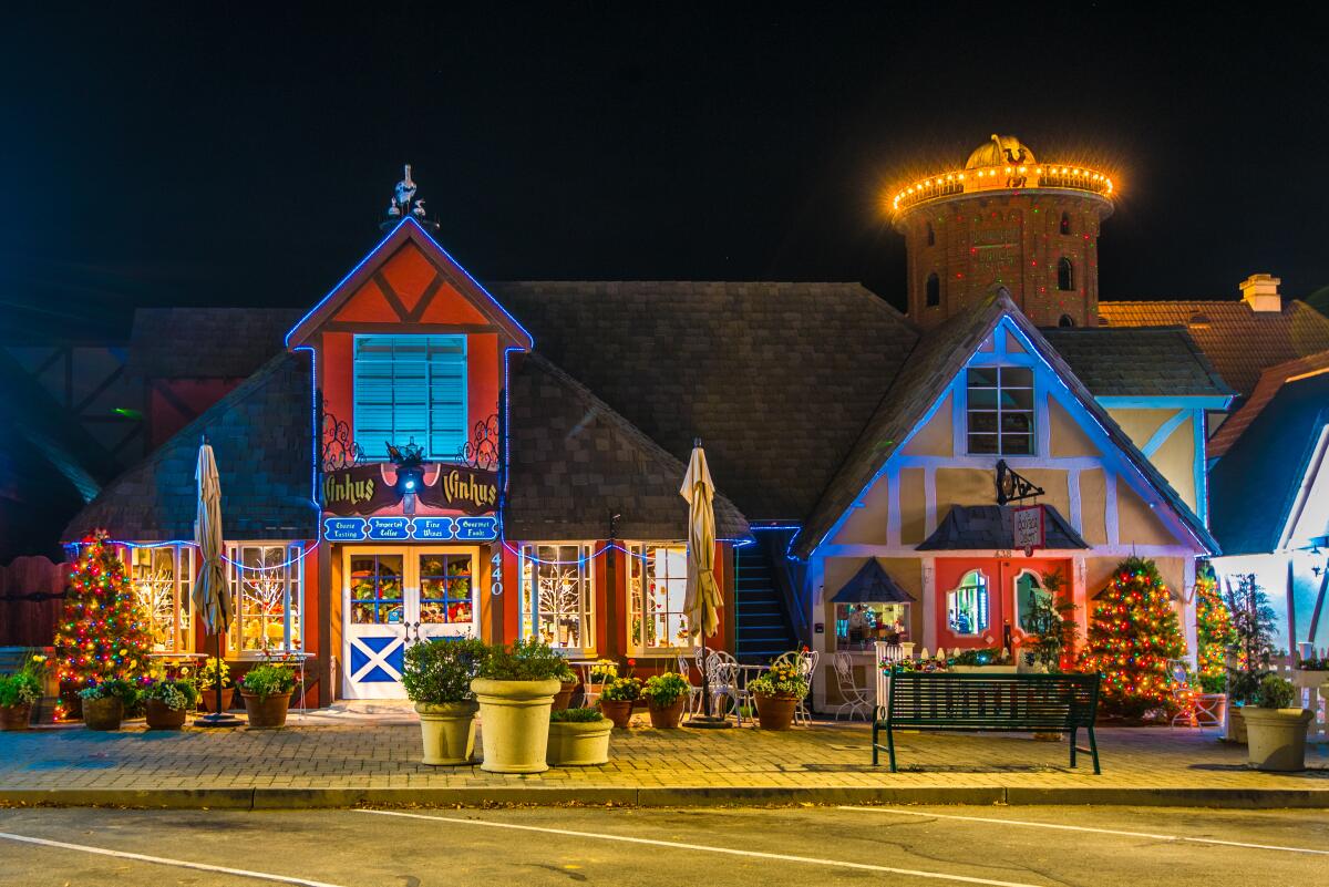 Peaked-roof storefronts with holiday lights and lighted Christmas trees in front.