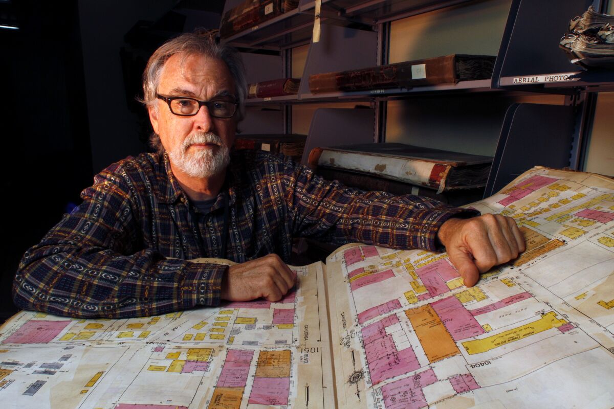 A man wearing glasses and sitting in an office has a map spread out in front of him.