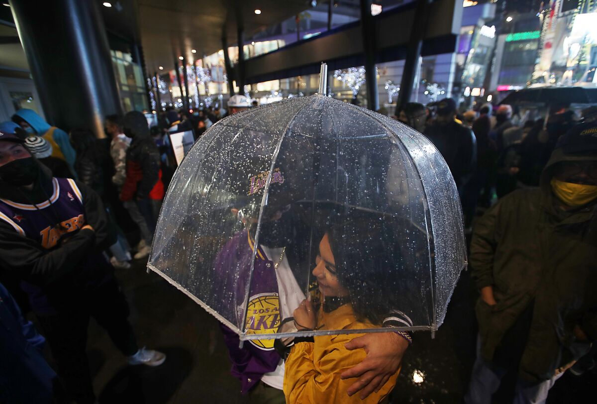A couple stand in the rain beneath an umbrella.