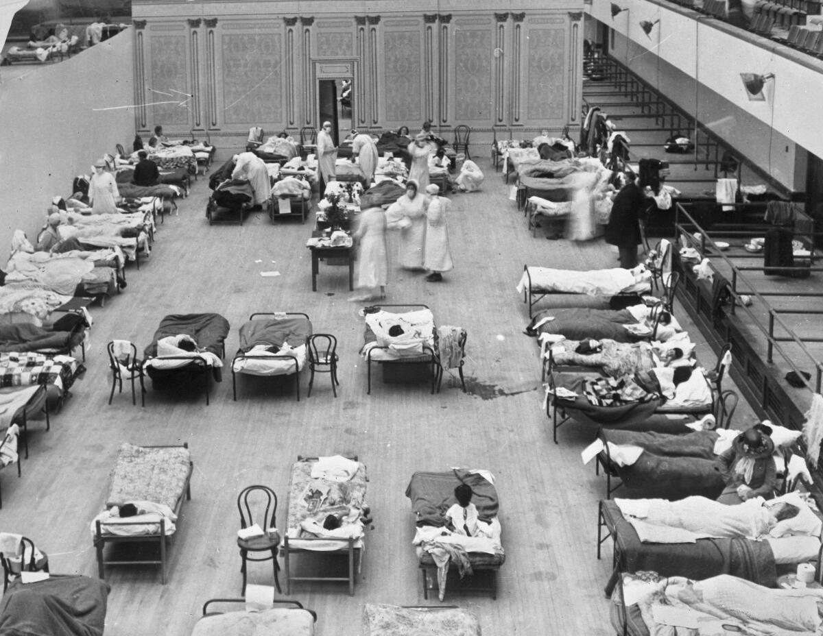 In a 1918 photo, volunteer nurses from the American Red Cross tend to influenza patients in the Oakland Municipal Auditorium, used as a temporary hospital.