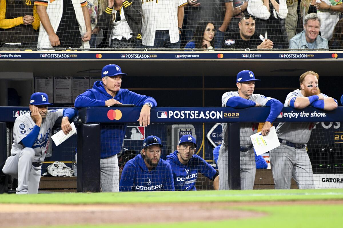 Dodgers players and coaches watch a playoff game against the Padres from the dugout railing and bench.