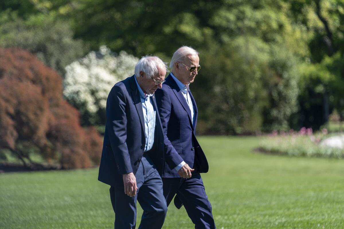 President Biden and Senator Bernie Sanders walk across the South Lawn of the White House.