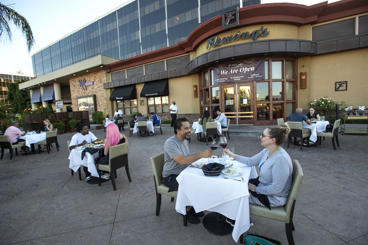 People eat at several tables spaced out in front of Fleming's restaurant entrance