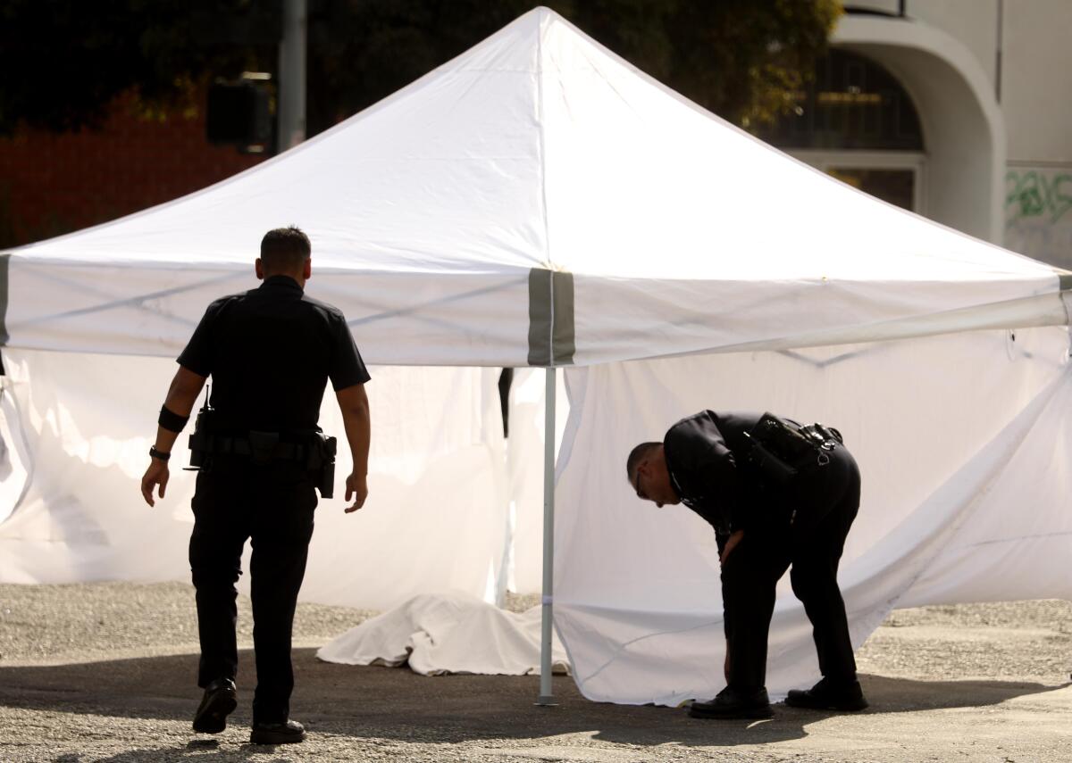 Two police officers, one standing and one bending over, next to a canopy over a body covered by a white sheet
