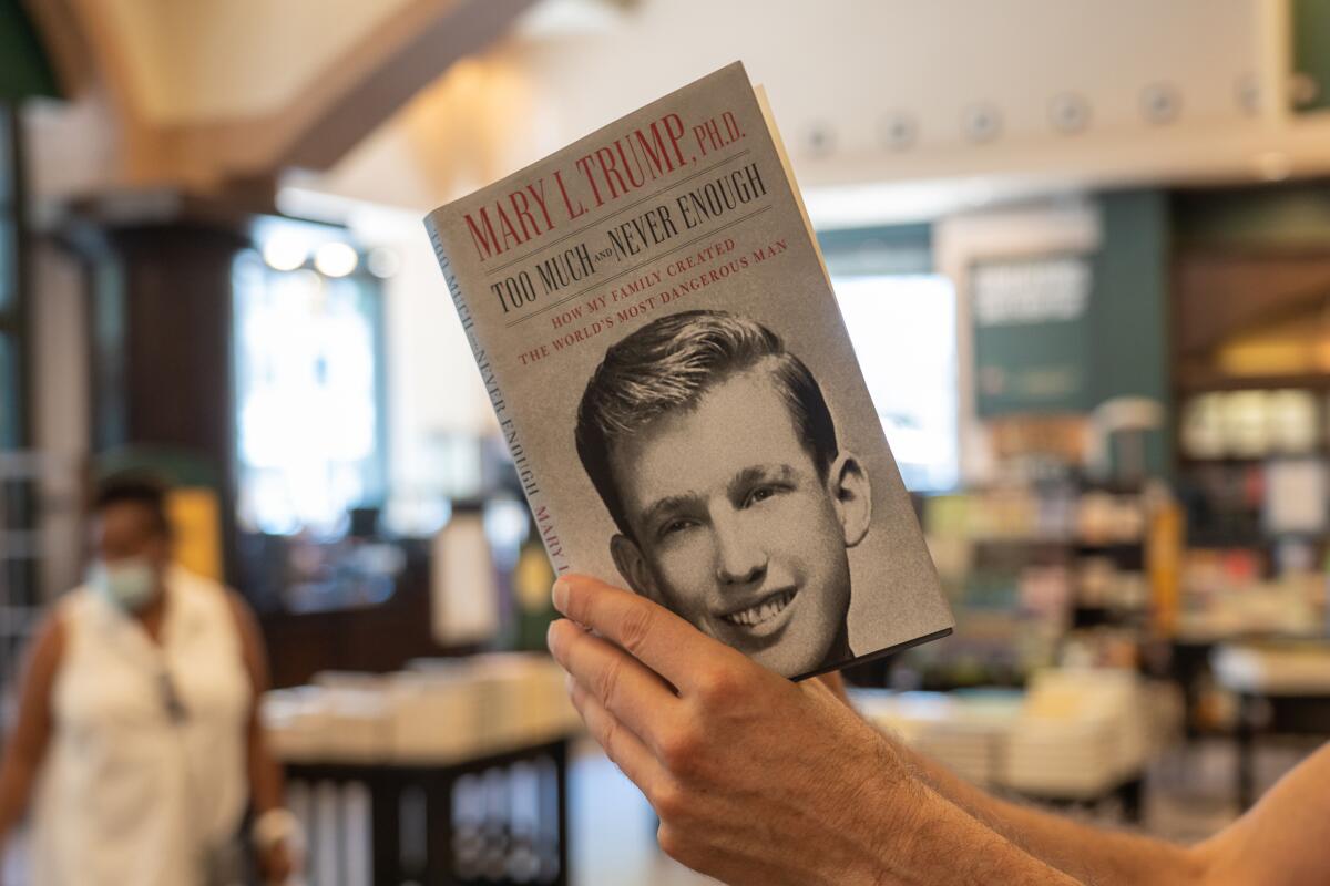 A person holds Mary Trump's book "Too Much and Never Enough," with a photo on the front of a young Donald Trump.