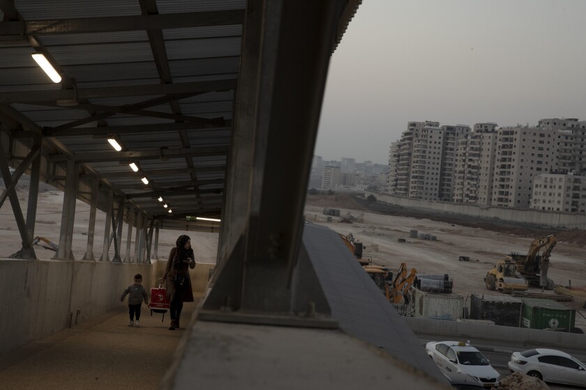 FILE - A woman and her child walk on a pedestrian ramp to the Qalandia checkpoint to the West Bank from Jerusalem, next to the site where Israel planned to build a massive Jewish settlement on the site of a long-abandoned airport, Nov. 24, 2021. An Israeli monitoring group said Monday, Dec. 6, 2021, that Jerusalem municipal officials have frozen plans to build a large Jewish settlement at the abandoned airport in east Jerusalem in the wake of heavy U.S. opposition to the project. (AP Photo/Maya Alleruzzo, File)