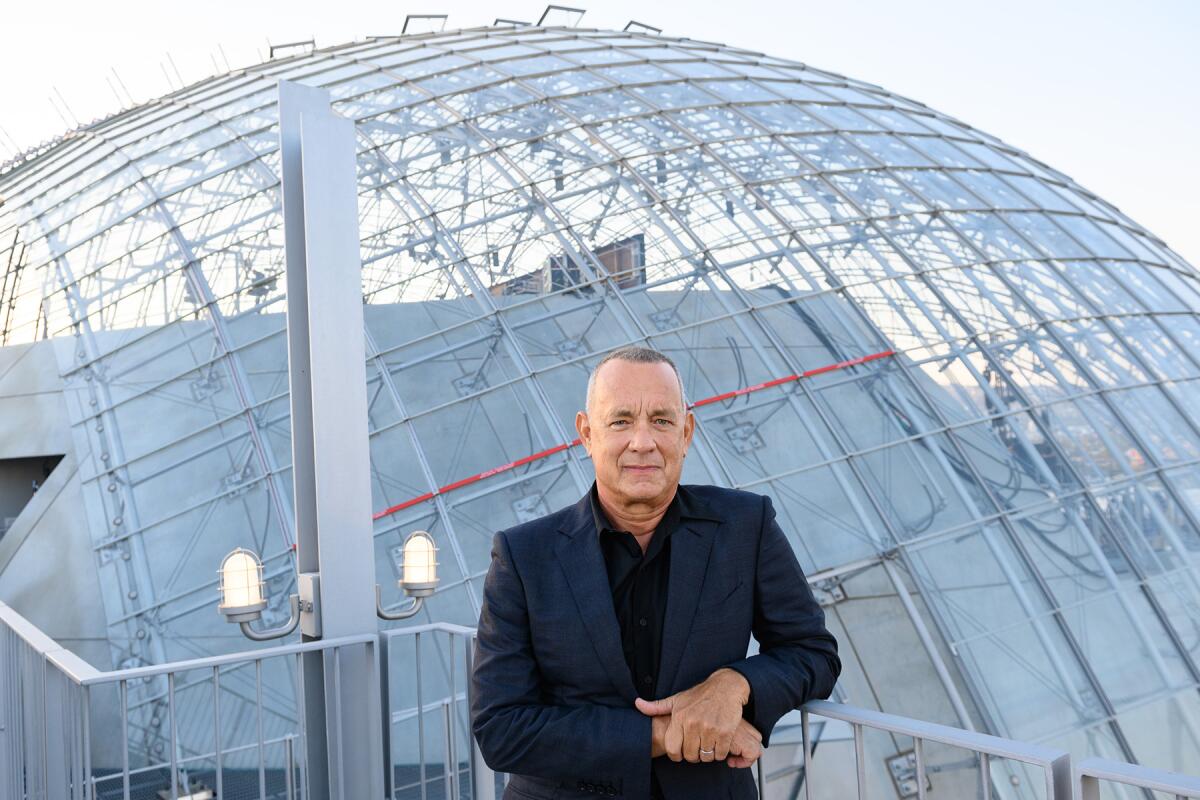 Tom Hanks stands in front of the Academy Museum's spherical building.