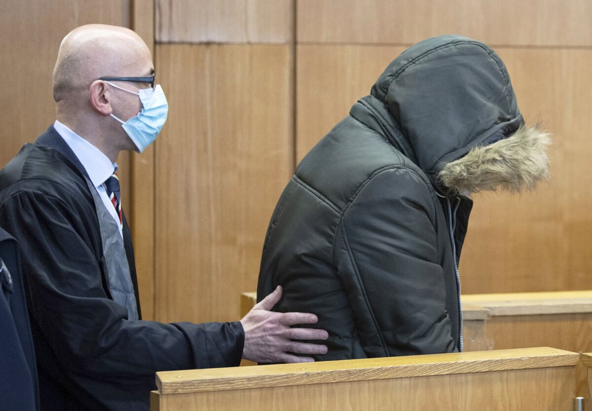 An unidentified Syrian doctor is led into the security room of the Higher Regional Court, by his lawyer Oussama Al-Agi, in Frankfurt, Germany, Wednesday, Jan. 19, 2022. A court in Germany will begin hearing a case against a Syrian doctor accused of crimes against humanity for torturing and killing inmates at a government-run prison in his home country. Federal prosecutors say the doctor worked at a military intelligence prison in the Syrian city of Homs from April 2011 until late 2012. Prosecutors accuse him of killing one person and torture in 18 cases. (Boris Roessler/Pool Photo via AP)