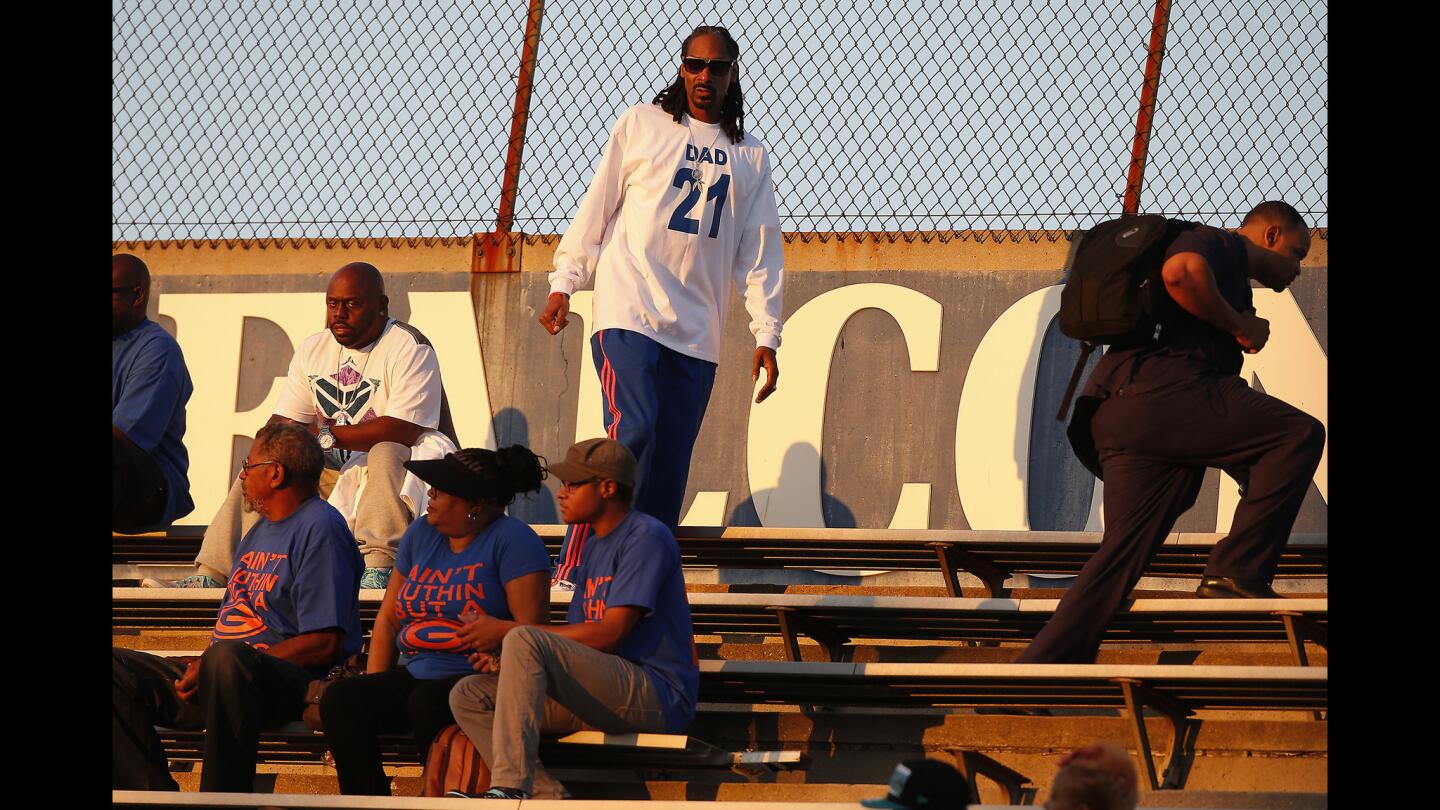 Snoop Dogg, aka Snoop Lion, finds a seat in the stands as his son, Cordell Broadus, prepares to play for Bishop Gorman against Servite in a game at Cerritos College on Friday night.