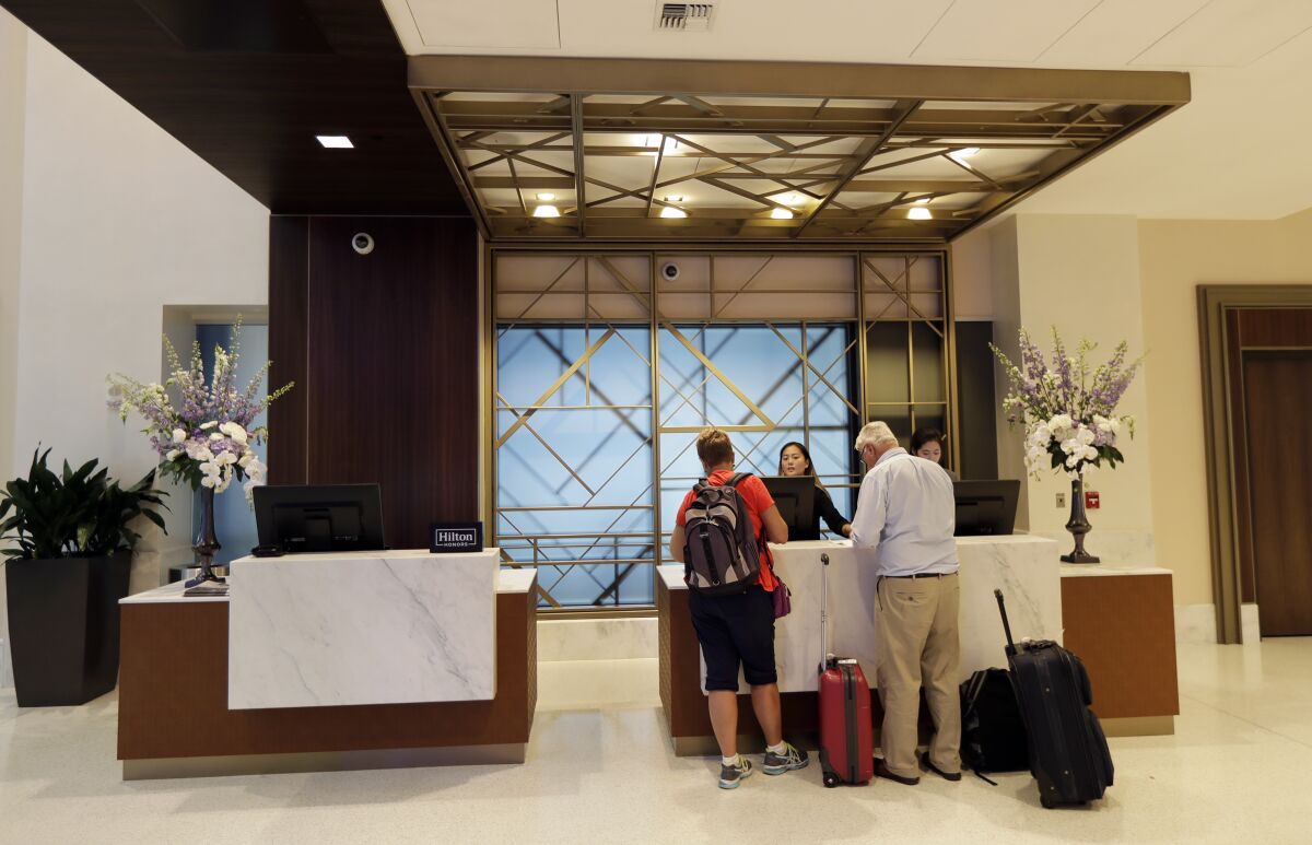FILE- In this Sept. 5, 2018, file photo guests stand at the front desk at the Embassy Suites by Hilton hotel in Seattle's Pioneer Square neighborhood in Seattle. Many major hotel chains are embracing all-inclusive offerings. For example, Hyatt recently announced an integration with AMR Collection brands, a group of about 100 all-inclusive resorts. Others, including Walt Disney World Resort, are workshopping the all-inclusive model, offering more specialized entertainment or outdoor access. These vacation packages are attractive to travelers in 2022, as paying for the bulk of travel expenses at once makes it easier to budget. For others, the opulence coupled with the minimal headache of planning every component of a trip is worth the higher price tag. (AP Photo/Ted S. Warren, File)