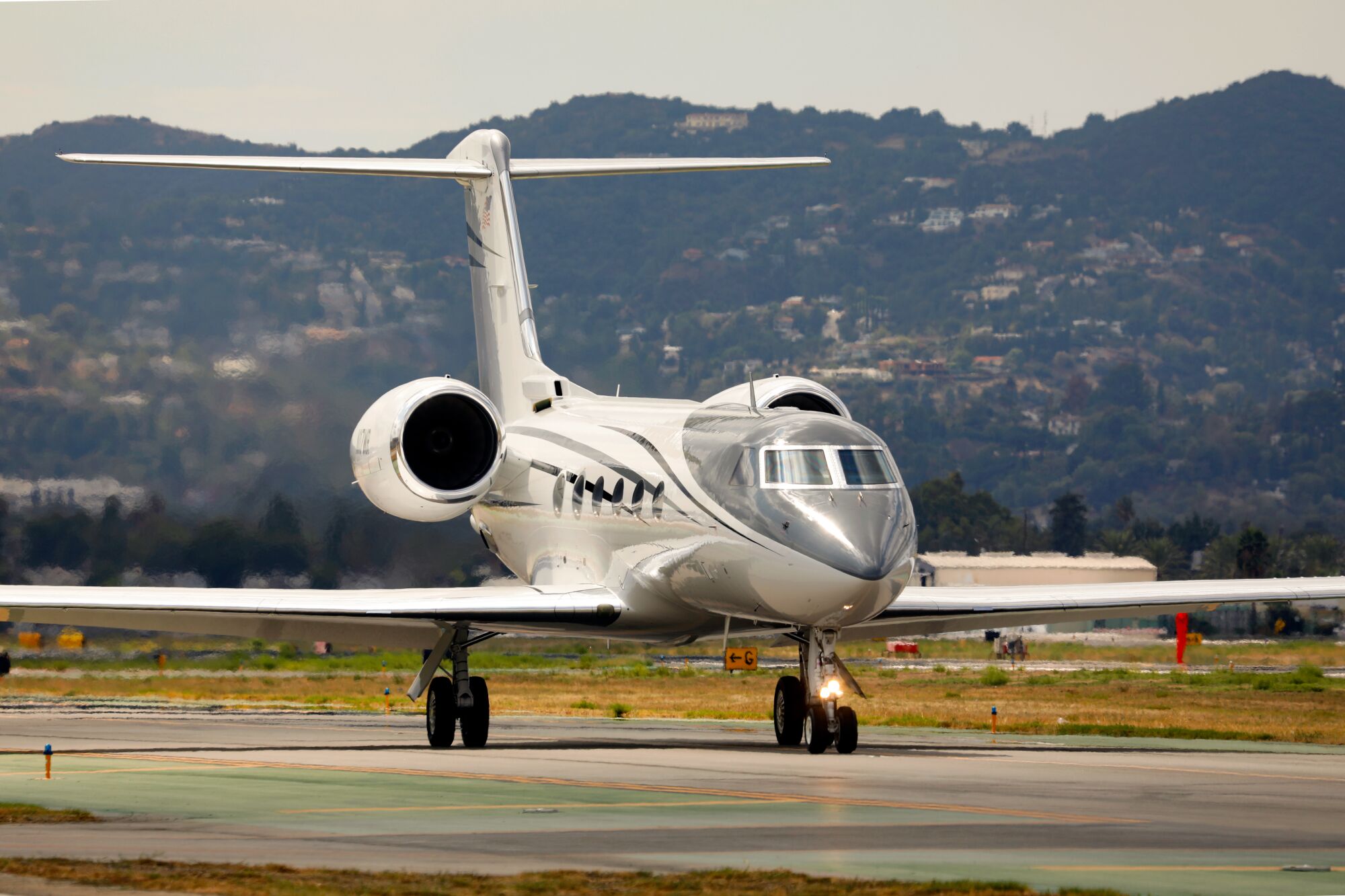 A jet taxis onto a runway at VNY in preparation for takeoff, within view of the Hollywood Hills.