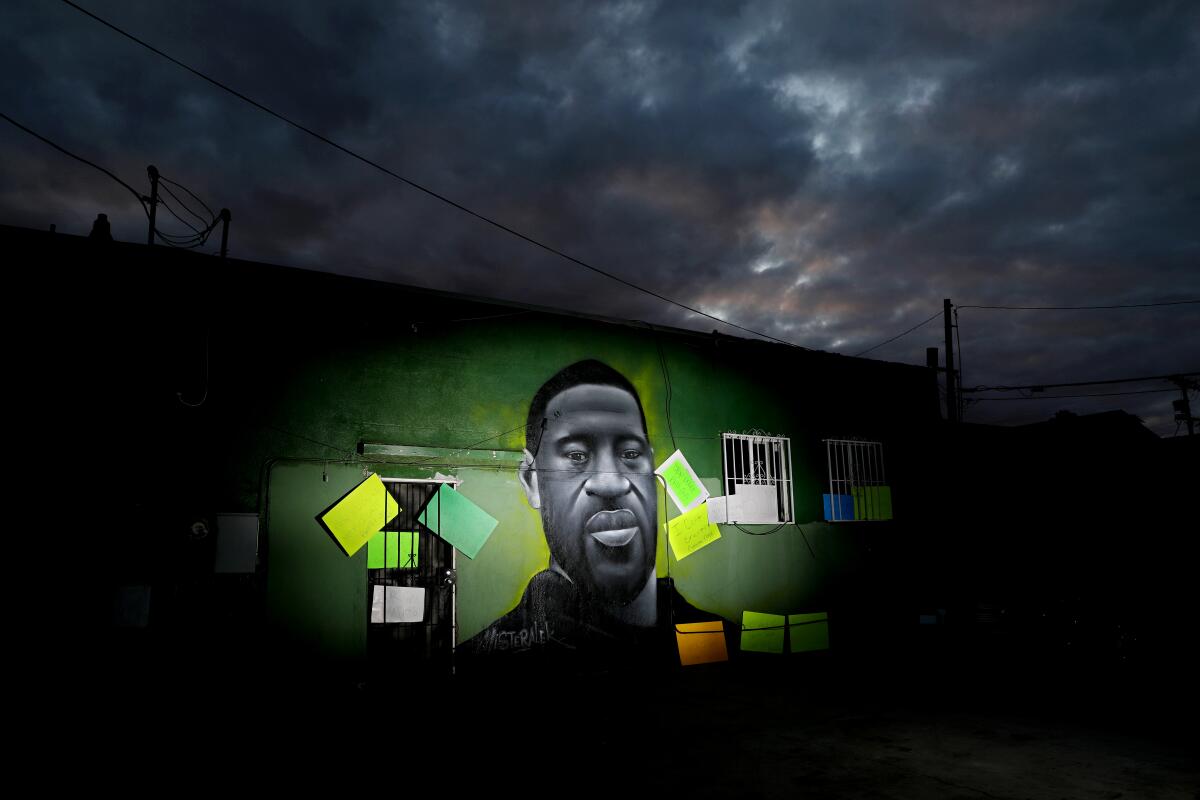 A mural of George Floyd on the side of a building is illuminated at night