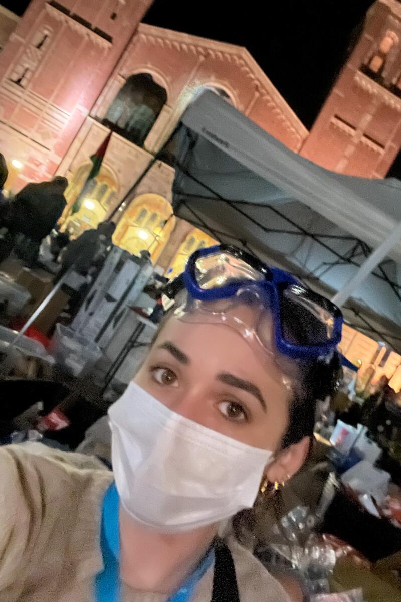 A selfie of a young woman in a paper mask with goggles on her head.