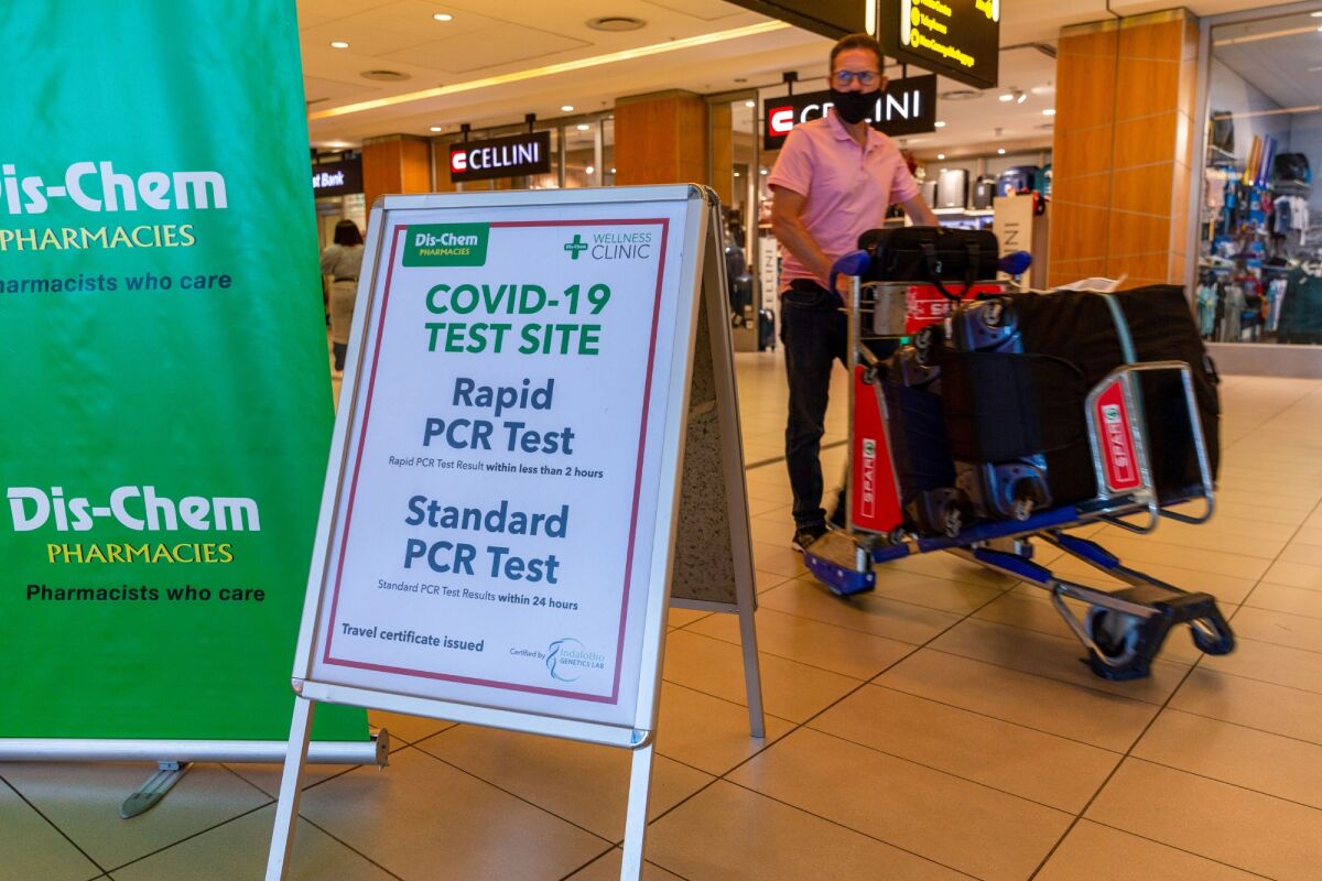 A man pushes luggage past a Covid-19 test site sign at Cape Town International Airport in South Africa on Dec. 3, 2021.