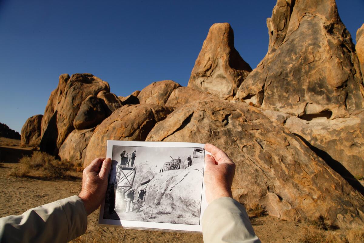 A person holds up a photo in front of a rock formation.