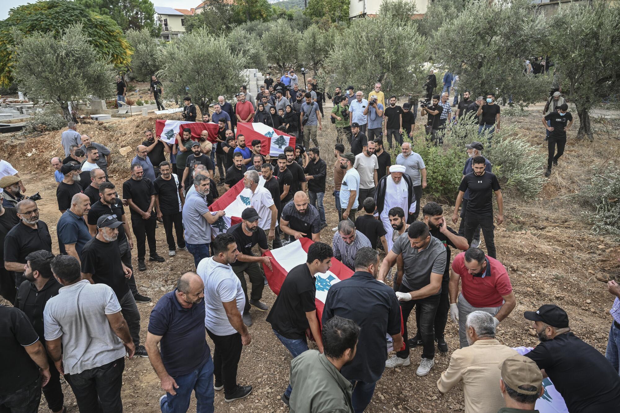 People in a field carry coffins covered in Lebanese flags. 