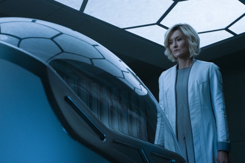A woman in a white coat looks down at a futuristic pod