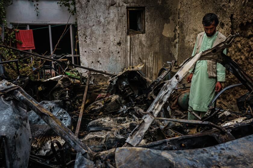 KABUL, AFGHANISTAN -- AUGUST 30, 2021: Relatives and neighbors of the Ahmadi family gathered around the incinerated husk of a vehicle targeted and hit earlier Sunday afternoon by an American drone strike, in Kabul, Afghanistan, Monday, Aug. 30, 2021. (MARCUS YAM / LOS ANGELES TIMES)