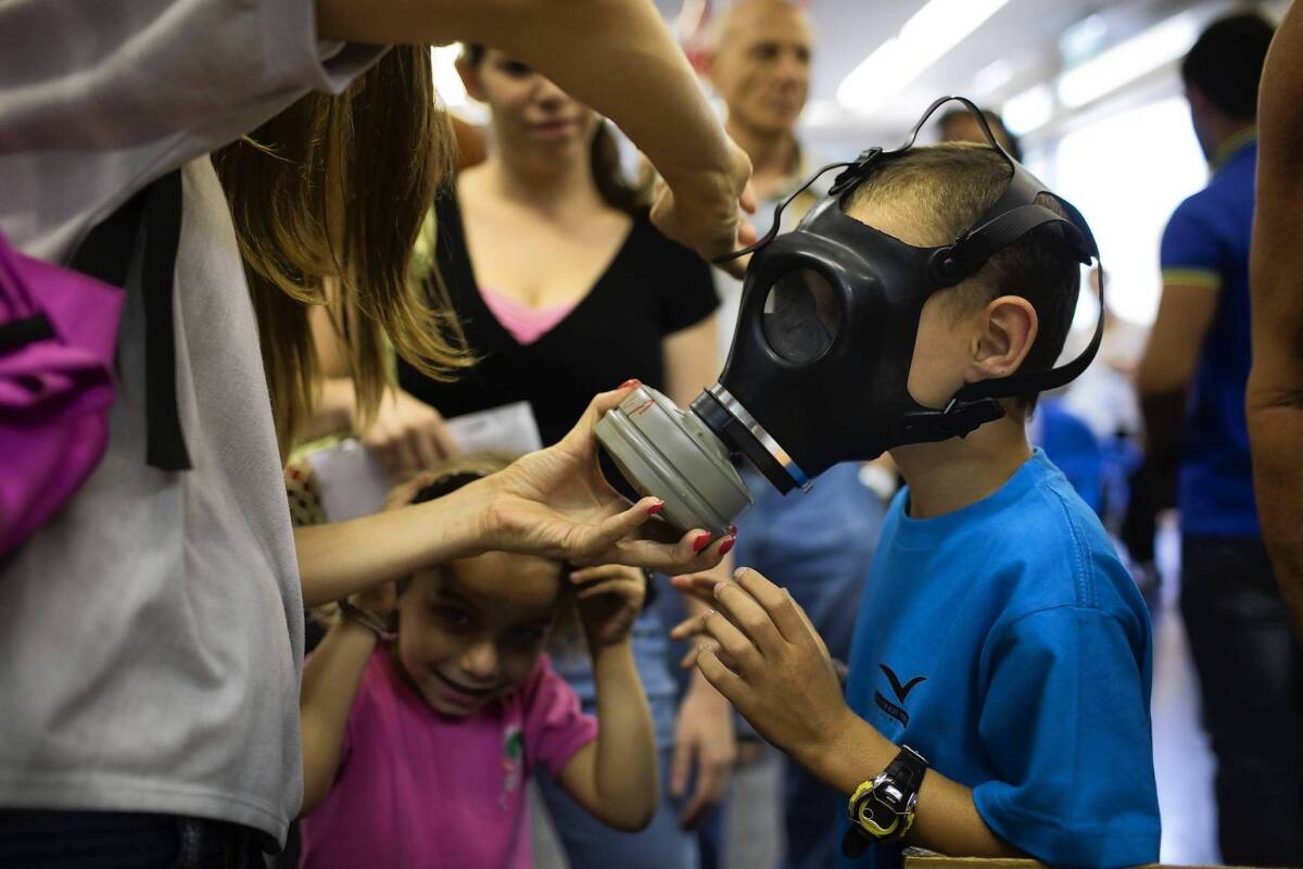 A woman shows a child how to put on a gas mask at a distribution center in Tel Aviv. Israelis are bracing for an attack after Syria vowed to strike Israel if Syria is struck by the United States.