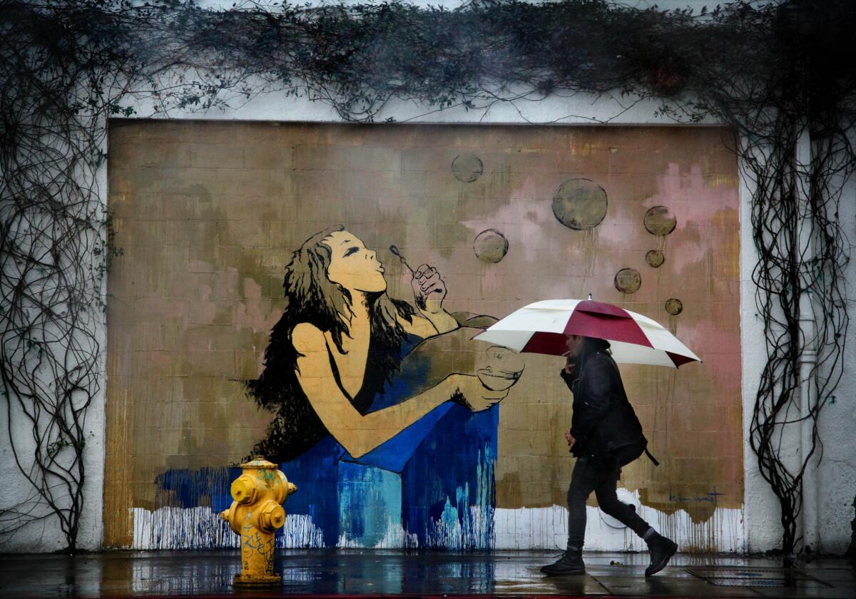 A pedestrian walks in the rain past a mural on South Hewitt Street in the Arts District of Los Angeles in February.
