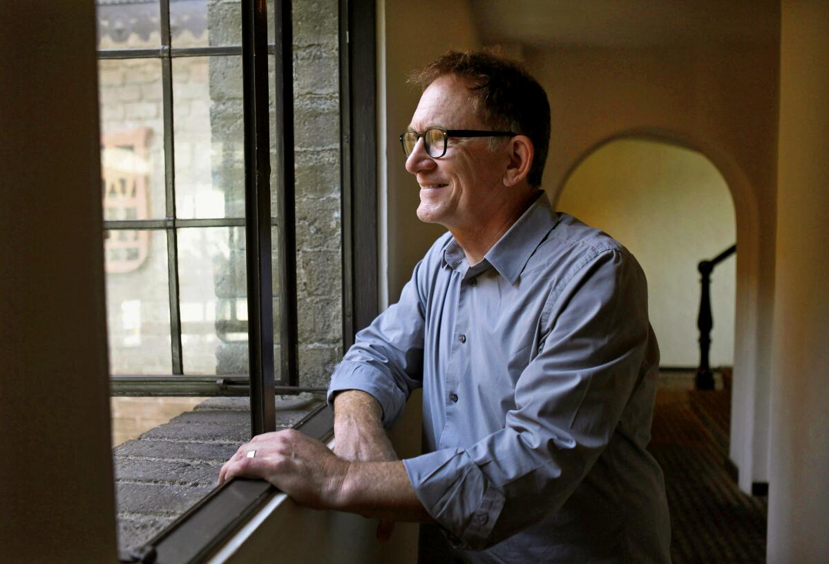 A man sits, looking out a window.