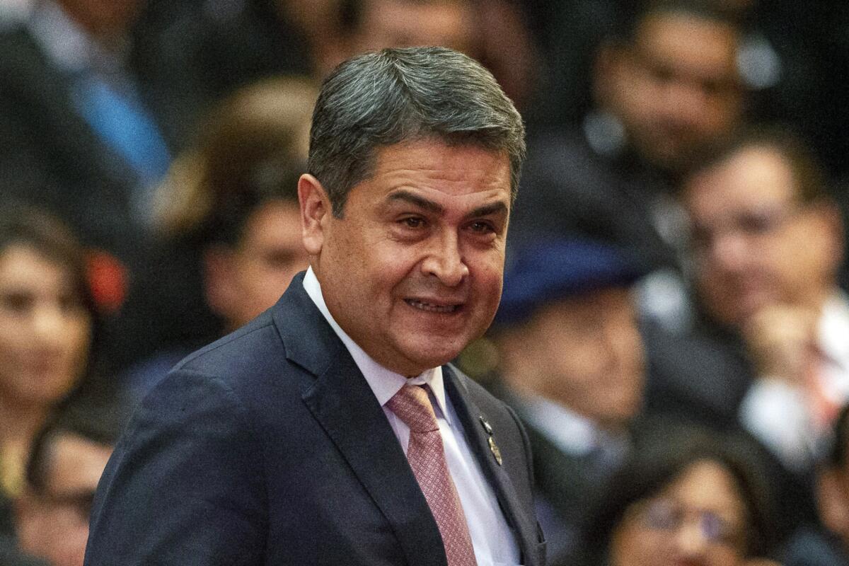 Honduras' President Juan Orlando Hernandez stands in front of a group of seated people.