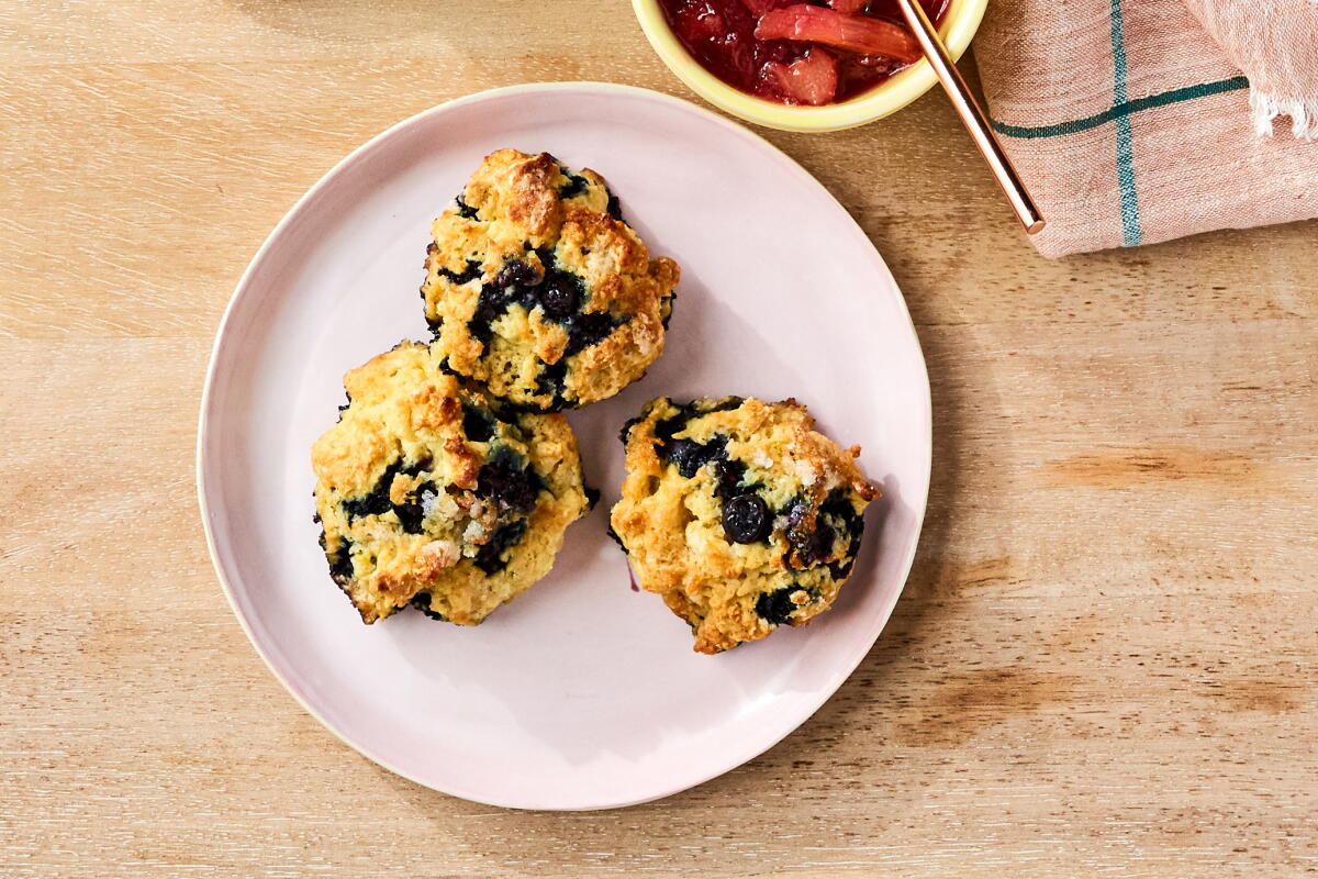 Three blueberry biscuits piled on a plate next to a bowl of rhubarb compote