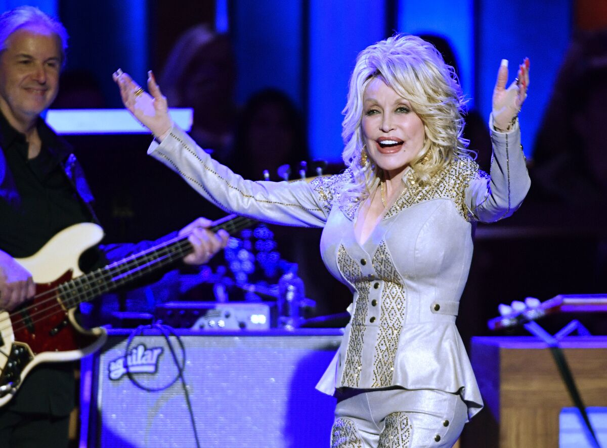 Dolly Parton shown on stage wearing a silver pants suit