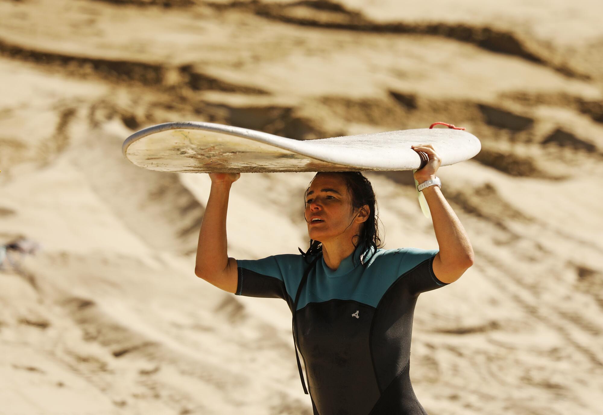 Natalia Folcini carries her surfboard at Surfrider Beach in Malibu.